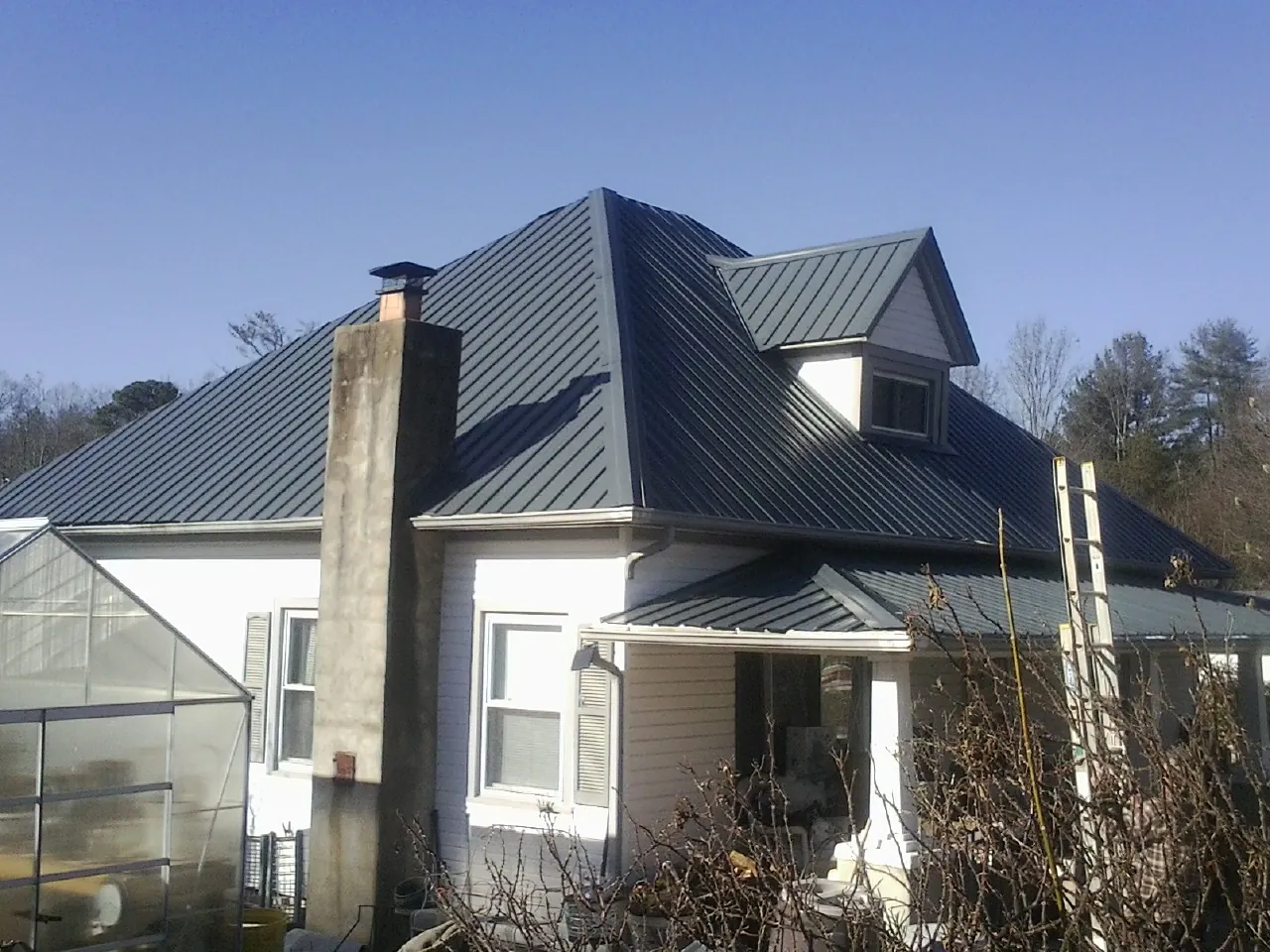 Dark blue standing seam metal roof on a white farmhouse with dormer — Slate & Tile Roof Repair by Roofing Brothers in Cedar Rapids