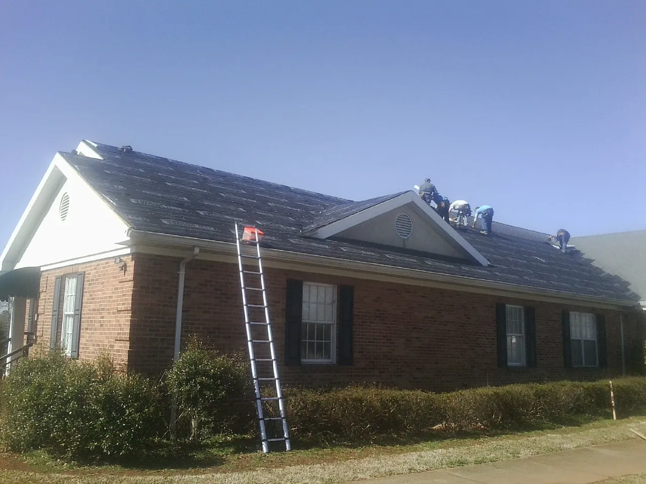 Crew tearing shingles off a brick ranch roof with a ladder set — Metal Roof Repair work by our crew in Cedar Rapids