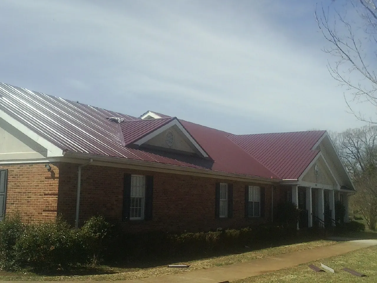 Red metal roof with gabled entries on a long brick building, from a Hail Damage Roof Repair job in Cedar Rapids