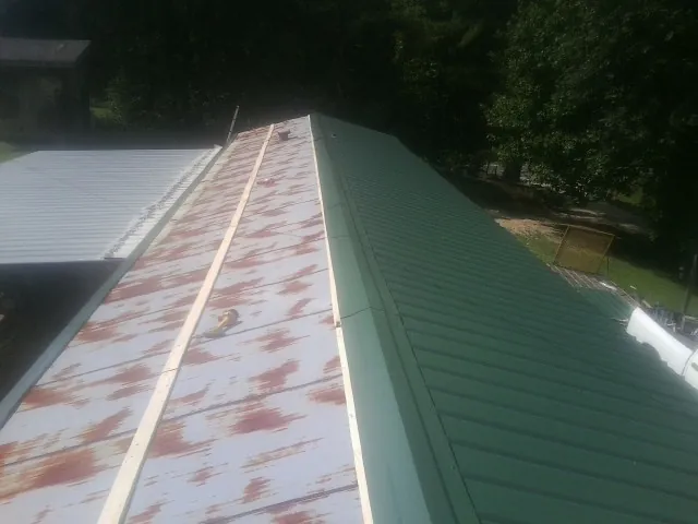 Old rusted panels beside newly installed green metal roofing — Wind Damage Roof Repair by Roofing Brothers in Cedar Rapids
