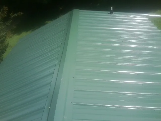 New green metal panels meeting at the ridge of a roof — Flat Roof Repair work by our crew in Cedar Rapids