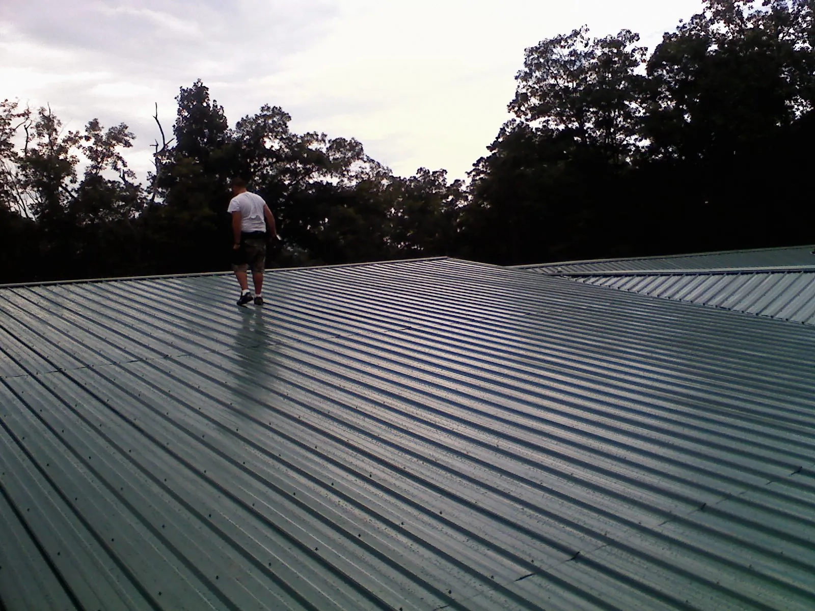 Roofer walking a wide expanse of new green metal roofing in Cedar Rapids