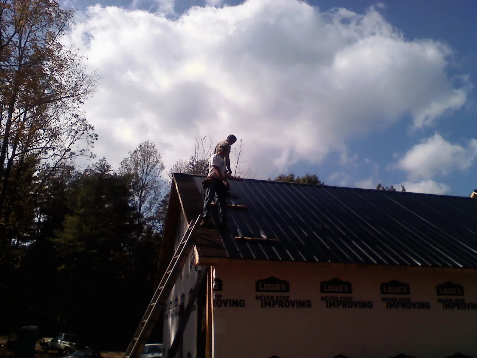 Roofer fastening dark metal panels high against a cloudy sky, from a Roof Inspection job in Cedar Rapids