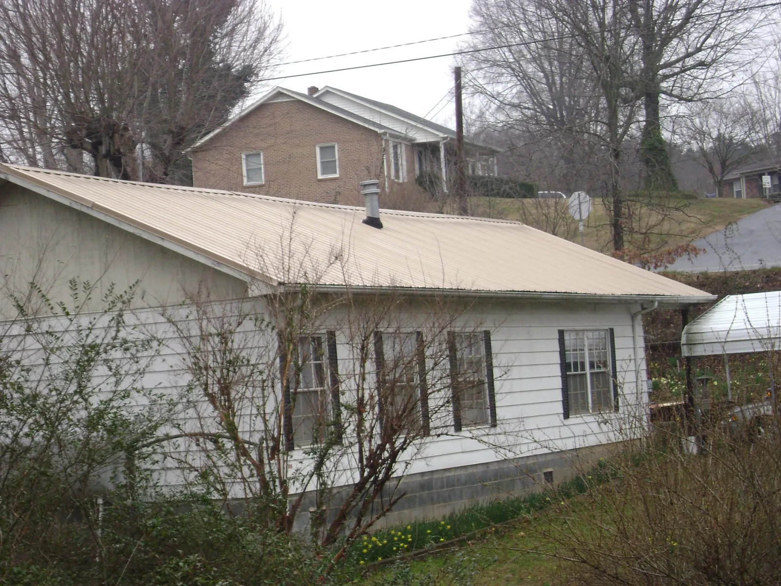 Tan metal roof on a white sided house set into a hillside — Commercial Roofing by Roofing Brothers in Cedar Rapids