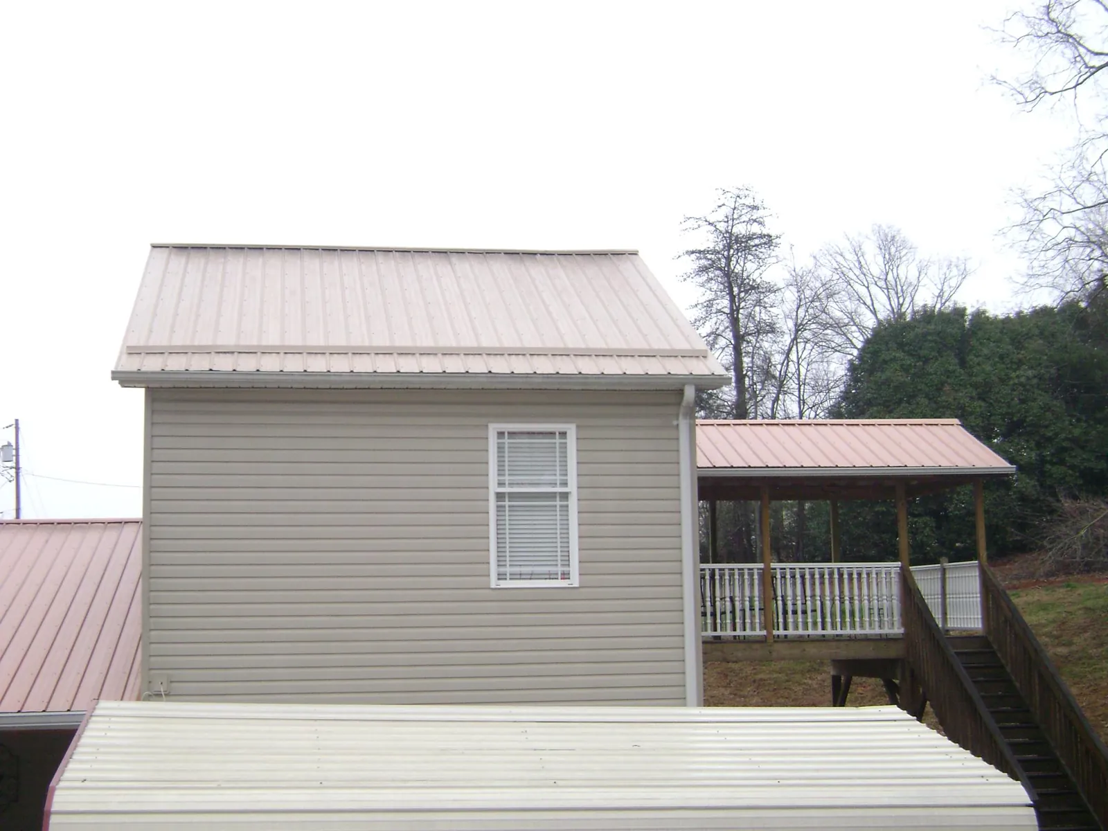 Tan metal roofs on a two story addition and attached porch, from a Roof Replacement job in Cedar Rapids