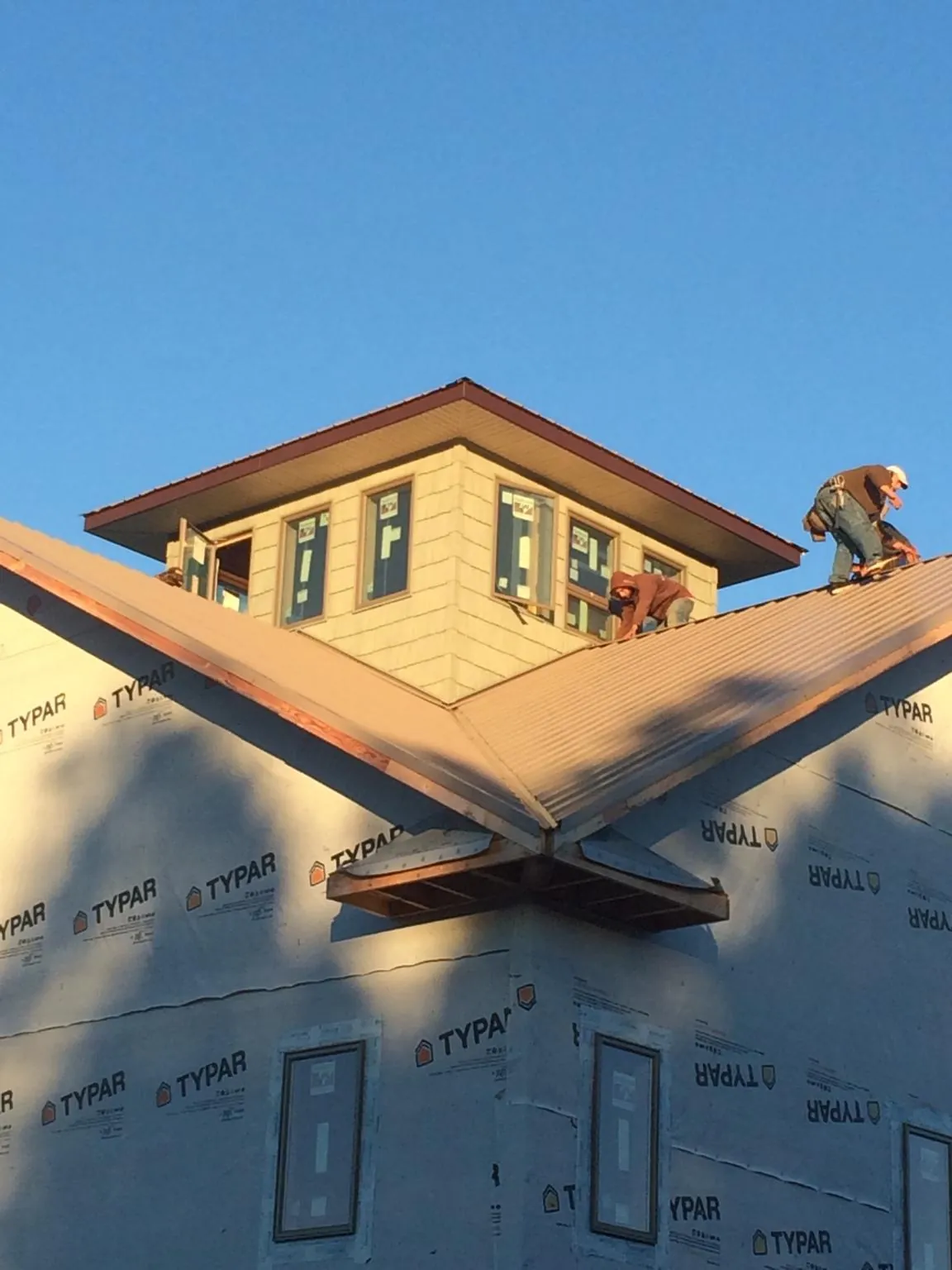 Roofers working around a rooftop cupola on a new metal roof at sunset — Roof Waterproofing in Cedar Rapids by Roofing Brothers